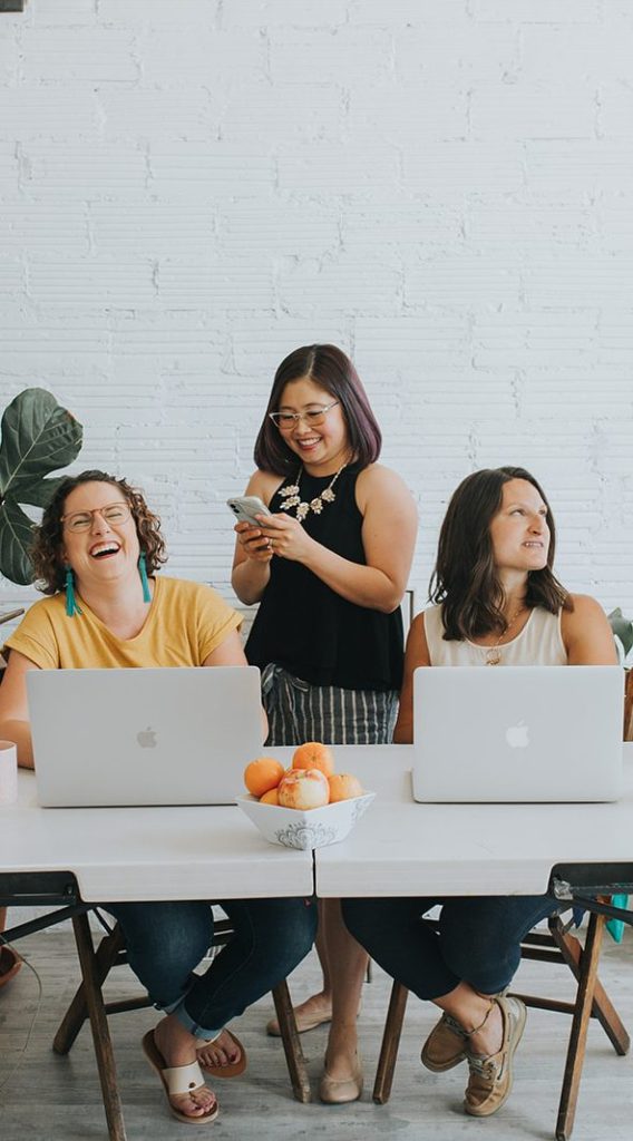 a few of the team laughing while working on computers and phones at a table